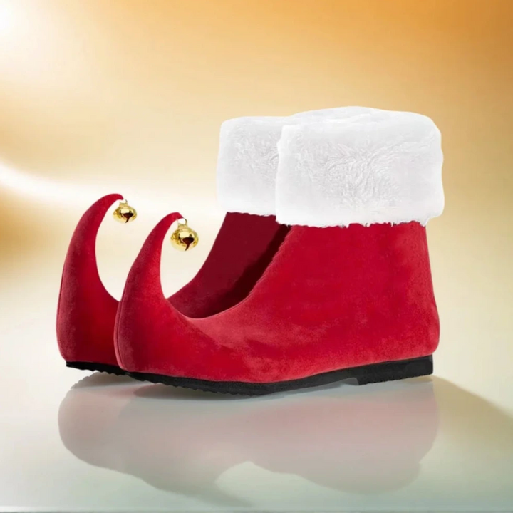 Red velvet slippers with white fur trim and gold bells on a reflective surface.